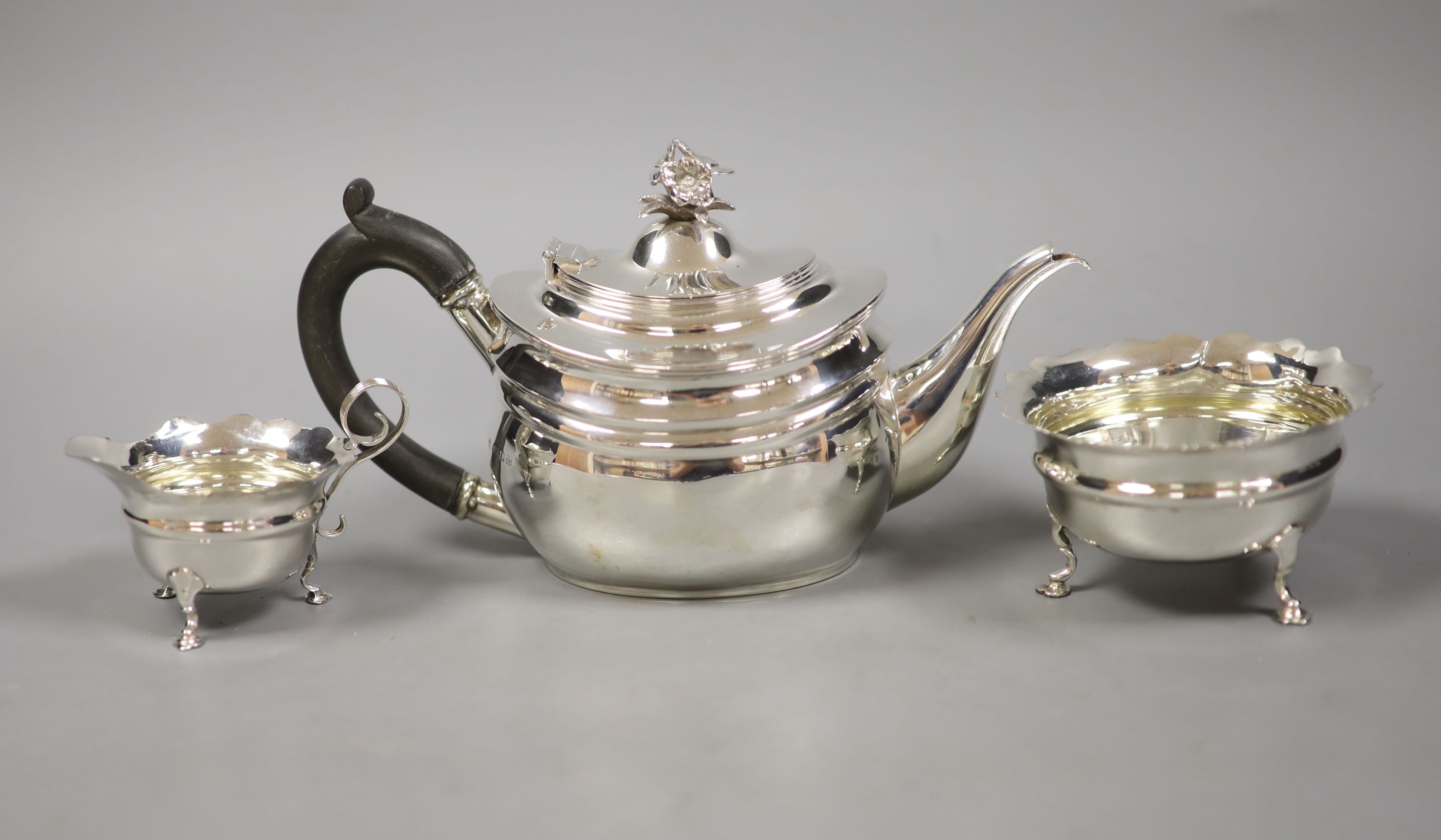 A George V silver teapot with floral finial, London, 1927 together with an associated cream jug, Chester 1907 and an Art Deco silver small dish